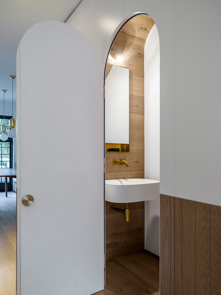 Transitional powder room in Sydney with multi-coloured walls, light hardwood floors, a wall-mount sink and brown floor.