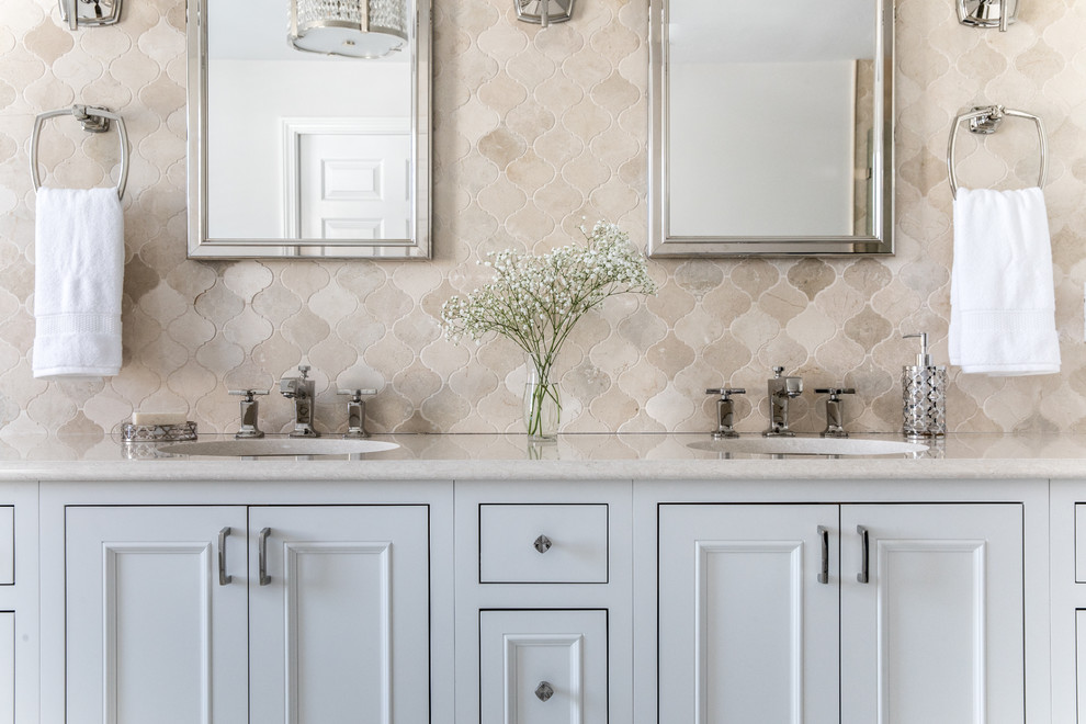 Example of a transitional master beige tile and mosaic tile marble floor and gray floor freestanding bathtub design in Boston with recessed-panel cabinets, white cabinets, a one-piece toilet, white walls, an undermount sink, quartz countertops, a hinged shower door and beige countertops