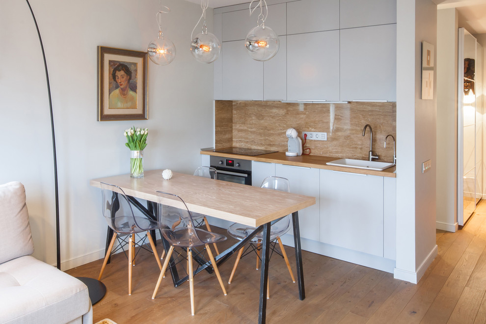 Small scandinavian single-wall eat-in kitchen in Berlin with a drop-in sink, flat-panel cabinets, white cabinets, wood benchtops, beige splashback, stainless steel appliances and light hardwood floors.