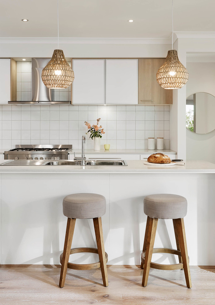 Inspiration for a contemporary kitchen in Melbourne with a double-bowl sink, flat-panel cabinets, white cabinets, white splashback, stainless steel appliances, light hardwood floors and with island.