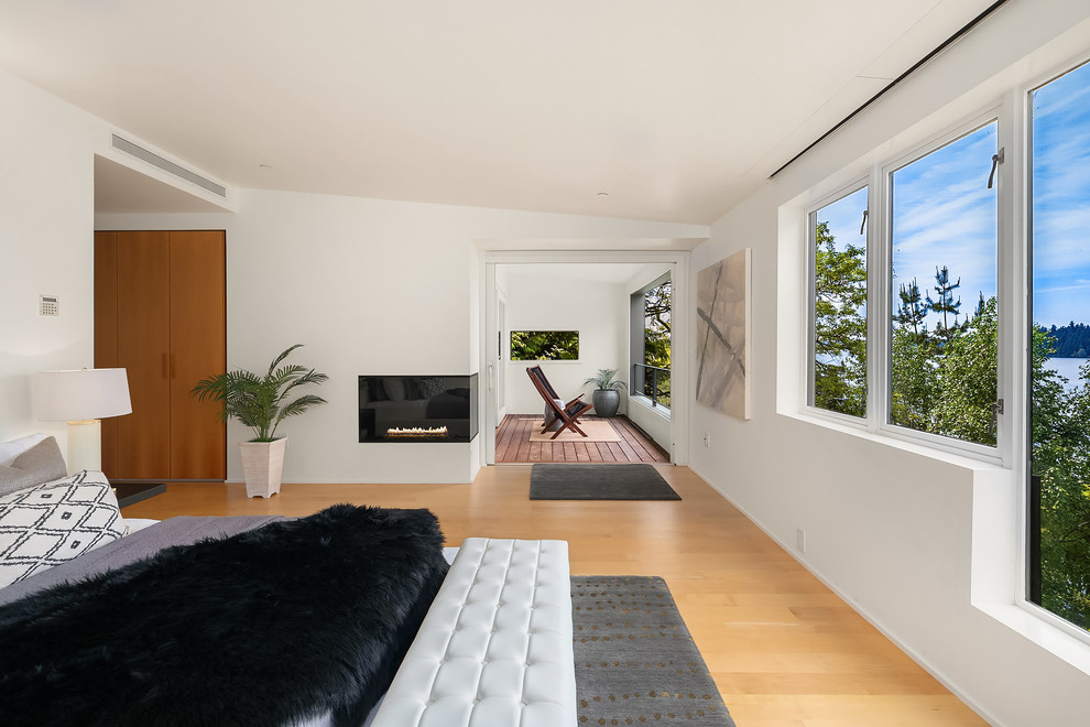 Photo of an expansive beach style master bedroom in Seattle with white walls, a corner fireplace, a plaster fireplace surround, medium hardwood floors and brown floor.