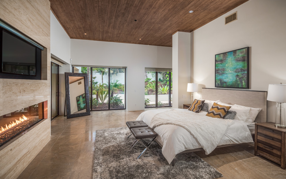 This is an example of an expansive contemporary master bedroom in San Diego with a ribbon fireplace, a stone fireplace surround, white walls and brown floor.