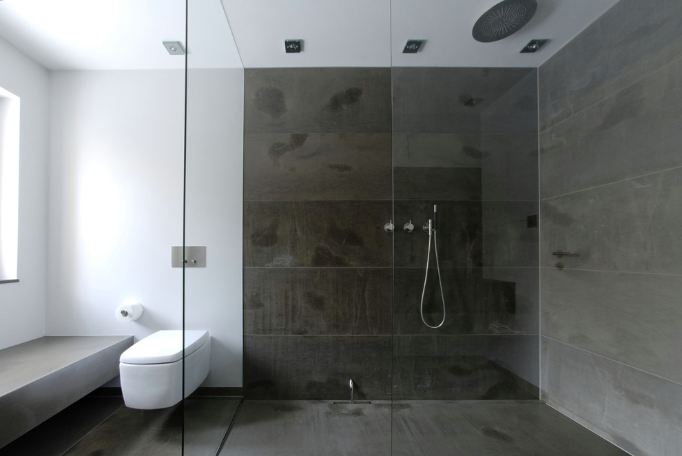 This is an example of a mid-sized contemporary 3/4 bathroom in Frankfurt with a wall-mount sink, a curbless shower, a wall-mount toilet, stone tile and white walls.