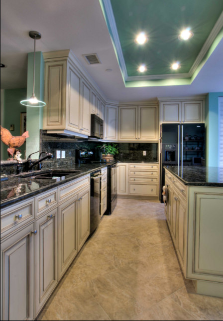 Inspiration for a mid-sized traditional l-shaped open plan kitchen in Tampa with a double-bowl sink, raised-panel cabinets, granite benchtops, black splashback, marble splashback, stainless steel appliances, linoleum floors, with island, beige floor, beige cabinets and black benchtop.