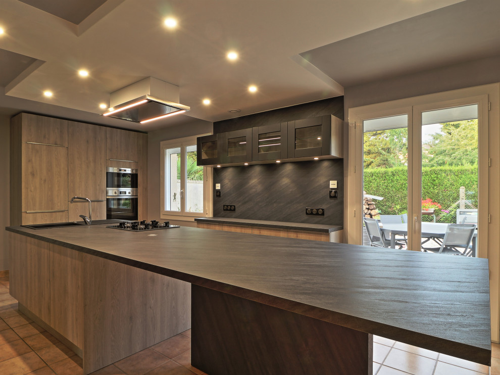 This is an example of a large modern single-wall eat-in kitchen in Other with an undermount sink, flat-panel cabinets, medium wood cabinets, limestone benchtops, black splashback, slate splashback, stainless steel appliances, limestone floors, with island, brown floor and black benchtop.