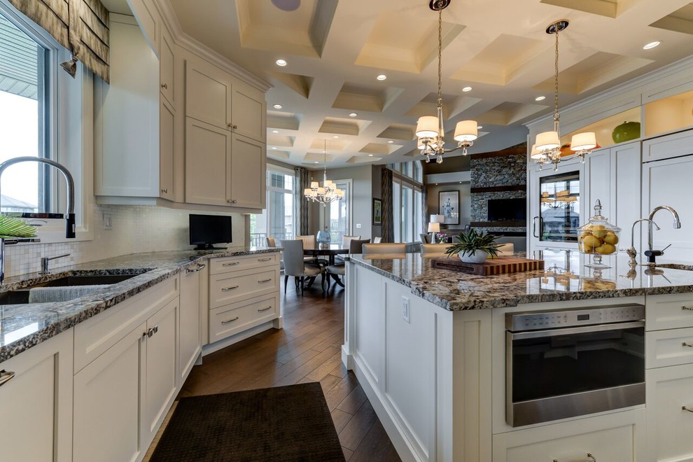 Example of a large transitional u-shaped medium tone wood floor and brown floor kitchen design in Edmonton with shaker cabinets, white cabinets, granite countertops, white backsplash, an island, an undermount sink, glass tile backsplash and paneled appliances