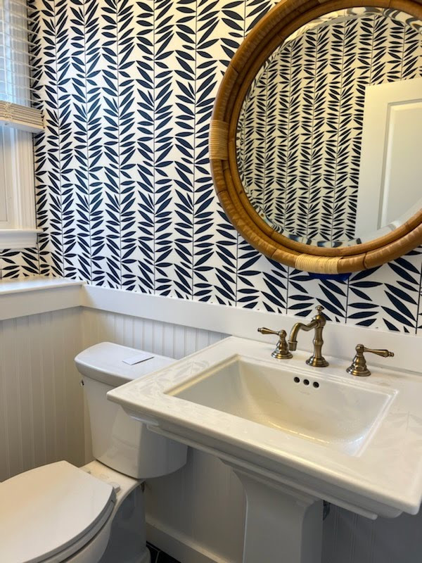 This is an example of a beach style cloakroom in Boston with white cabinets, blue walls, a pedestal sink, blue floors, a freestanding vanity unit and wallpapered walls.
