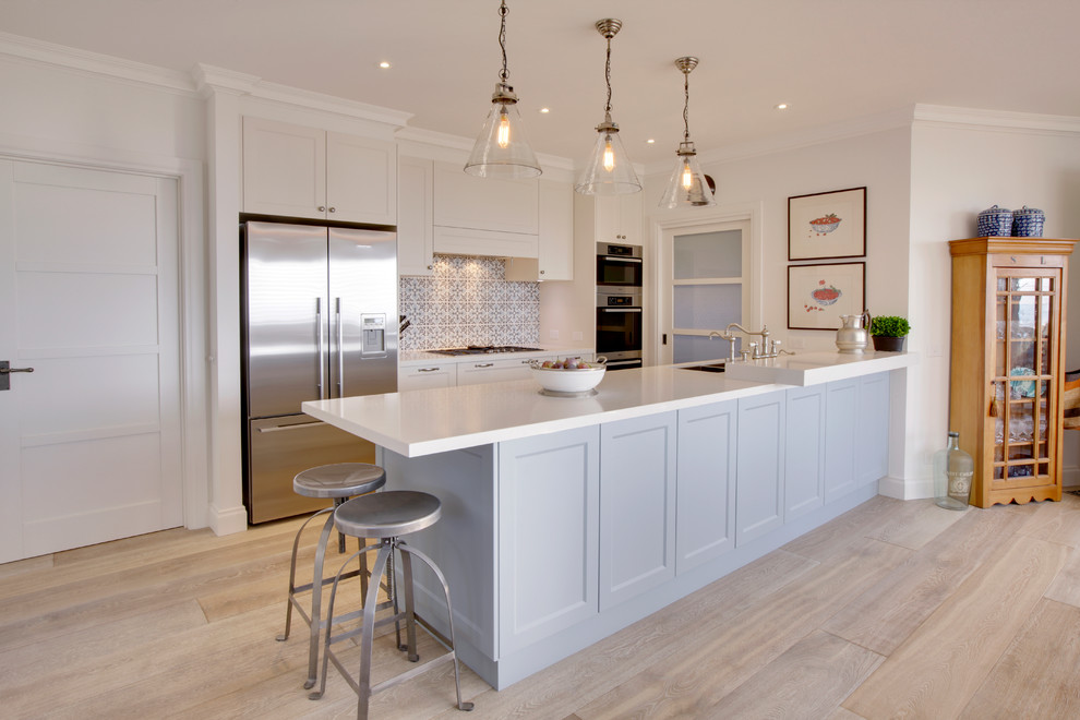 This is an example of a large beach style single-wall kitchen pantry in Melbourne with a double-bowl sink, beaded inset cabinets, white cabinets, solid surface benchtops, mosaic tile splashback, stainless steel appliances, plywood floors and with island.