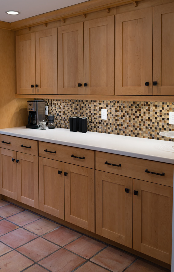 This is an example of a mid-sized eclectic u-shaped kitchen in Boston with an undermount sink, recessed-panel cabinets, light wood cabinets, solid surface benchtops, multi-coloured splashback, glass tile splashback, stainless steel appliances, terra-cotta floors and with island.