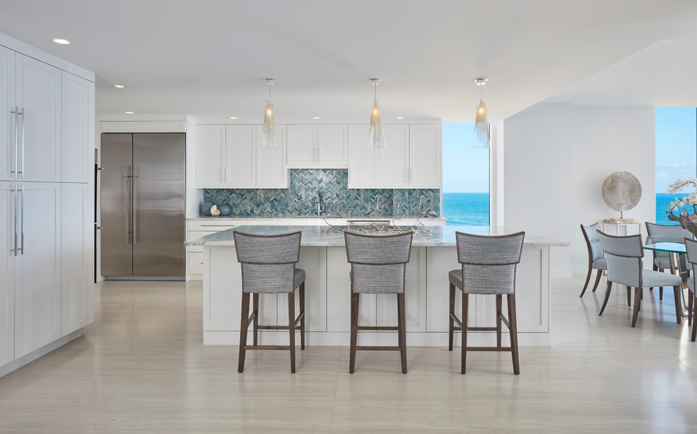 Inspiration for a large beach style l-shaped open plan kitchen in Miami with shaker cabinets, white cabinets, stainless steel appliances, with island, an undermount sink, marble benchtops, blue splashback, glass tile splashback, porcelain floors, grey floor and white benchtop.