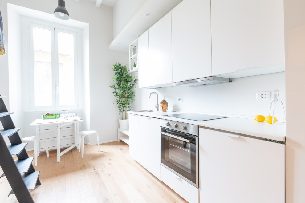 Inspiration for a small scandi single-wall open plan kitchen in Milan with light hardwood flooring, exposed beams, a single-bowl sink, flat-panel cabinets, white cabinets, laminate countertops, white splashback, stainless steel appliances, no island and white worktops.