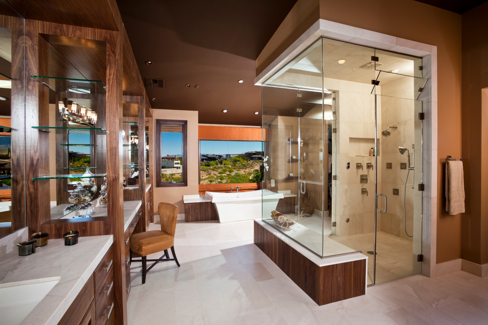 Photo of a large contemporary master bathroom in Las Vegas with a curbless shower, an undermount sink, flat-panel cabinets, medium wood cabinets, a drop-in tub, beige tile, stone tile, brown walls, marble floors and marble benchtops.