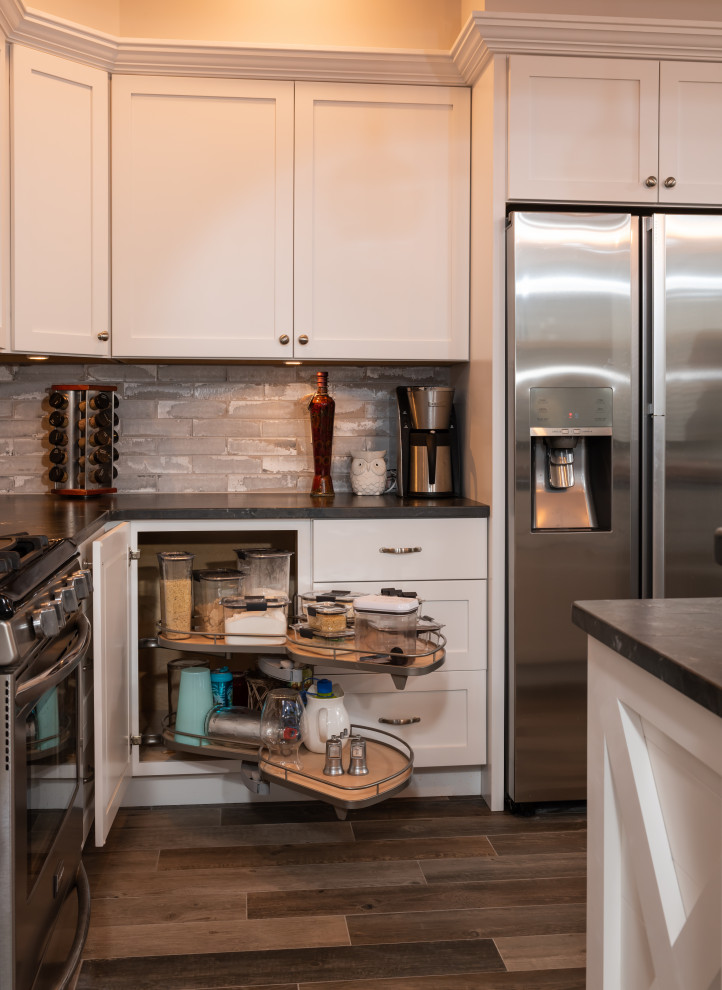Mid-sized mountain style l-shaped porcelain tile and gray floor open concept kitchen photo with an undermount sink, shaker cabinets, white cabinets, granite countertops, gray backsplash, brick backsplash, stainless steel appliances, an island and black countertops
