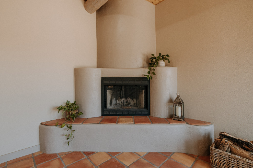 Cette photo montre un grand salon sud-ouest américain ouvert avec un mur beige, tomettes au sol, une cheminée d'angle, un manteau de cheminée en plâtre et un sol orange.