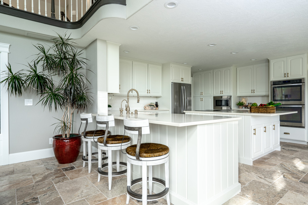 Open concept kitchen - transitional u-shaped travertine floor and brown floor open concept kitchen idea in Seattle with an undermount sink, raised-panel cabinets, white cabinets, quartz countertops, white backsplash, porcelain backsplash, stainless steel appliances, an island and white countertops