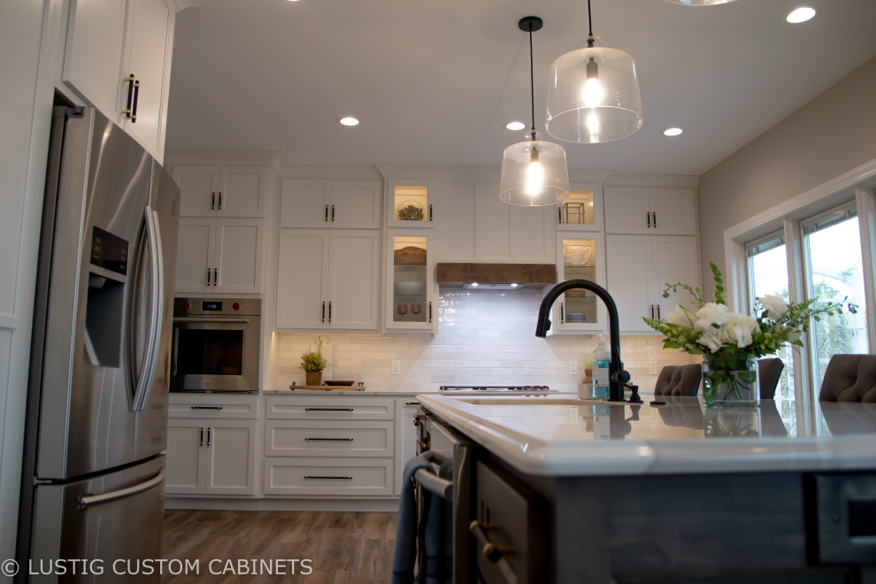 Inspiration for a large transitional l-shaped laminate floor and brown floor open concept kitchen remodel with an undermount sink, flat-panel cabinets, white cabinets, quartz countertops, white backsplash, ceramic backsplash, stainless steel appliances, an island and white countertops