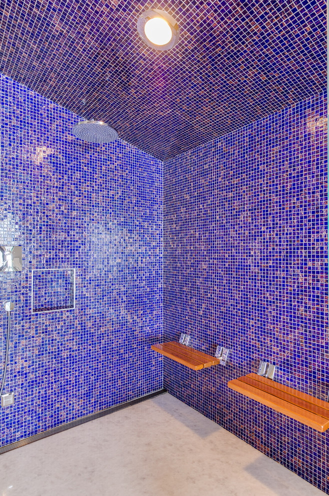 Photo of an expansive contemporary bathroom in Other with blue tile, multi-coloured tile, flat-panel cabinets, brown cabinets, a freestanding tub, a curbless shower, a wall-mount toilet, glass tile, grey walls, light hardwood floors, an undermount sink and granite benchtops.