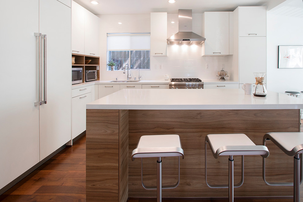 Mid-sized contemporary l-shaped eat-in kitchen in Los Angeles with a drop-in sink, flat-panel cabinets, medium wood cabinets, quartzite benchtops, white splashback, porcelain splashback, stainless steel appliances, laminate floors, with island, brown floor and white benchtop.