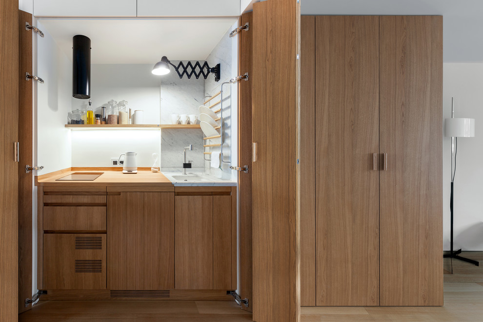 This is an example of a small contemporary single-wall kitchen in Moscow with an undermount sink, medium wood cabinets, wood benchtops, white splashback, panelled appliances, medium hardwood floors, flat-panel cabinets, brown floor and no island.