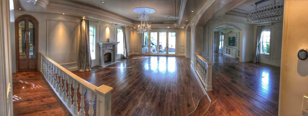 This is an example of a large formal open concept living room in Los Angeles with beige walls, medium hardwood floors, a standard fireplace, a stone fireplace surround, no tv, brown floor, recessed and panelled walls.