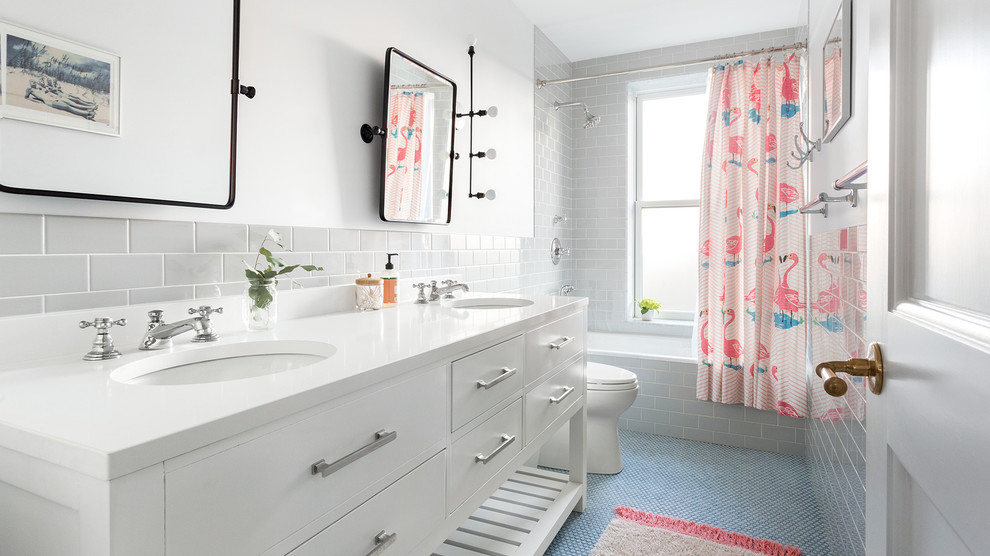 Photo of a transitional bathroom in New York with flat-panel cabinets, white cabinets, a drop-in tub, a shower/bathtub combo, gray tile, subway tile, white walls, mosaic tile floors, an undermount sink, blue floor, a shower curtain and white benchtops.