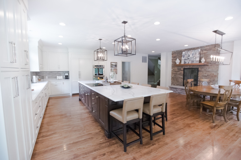 This is an example of a large arts and crafts galley open plan kitchen in Indianapolis with an undermount sink, shaker cabinets, white cabinets, quartzite benchtops, grey splashback, subway tile splashback, panelled appliances, medium hardwood floors, with island and brown floor.