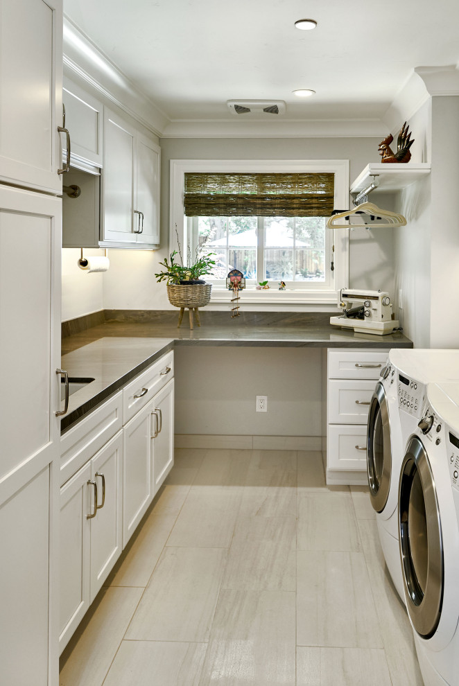 サンフランシスコにあるラグジュアリーな中くらいなトランジショナルスタイルのおしゃれな洗濯室 (ll型、アンダーカウンターシンク、シェーカースタイル扉のキャビネット、白いキャビネット、グレーのキッチンパネル、石スラブのキッチンパネル、グレーの壁、磁器タイルの床、左右配置の洗濯機・乾燥機、ベージュの床、グレーのキッチンカウンター、白い天井) の写真