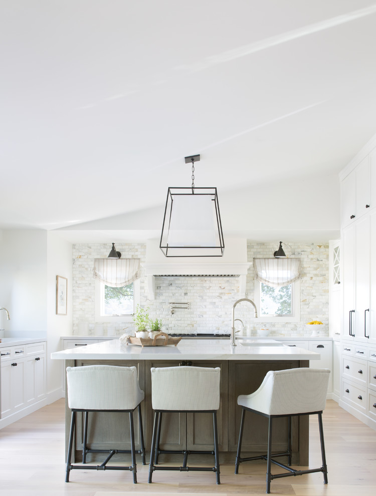 This is an example of a beach style kitchen in San Francisco with shaker cabinets, white cabinets, multi-coloured splashback, light hardwood floors, with island, beige floor and white benchtop.
