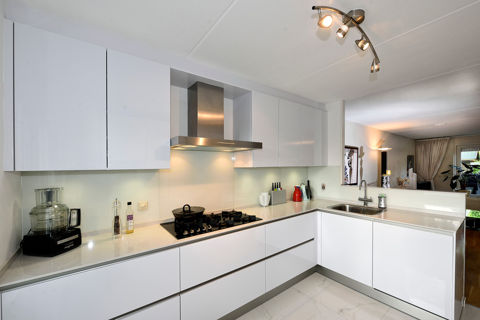 This is an example of a mid-sized contemporary l-shaped open plan kitchen in Other with an integrated sink, flat-panel cabinets, white cabinets, quartz benchtops, white splashback, glass sheet splashback, black appliances, porcelain floors and no island.