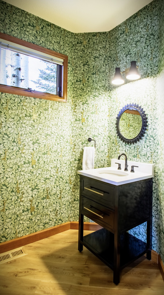 Exemple d'un petit WC et toilettes chic avec un placard avec porte à panneau encastré, des portes de placard noires, un mur vert, parquet clair, un lavabo intégré, un plan de toilette en quartz modifié, un plan de toilette blanc, meuble-lavabo sur pied et du papier peint.