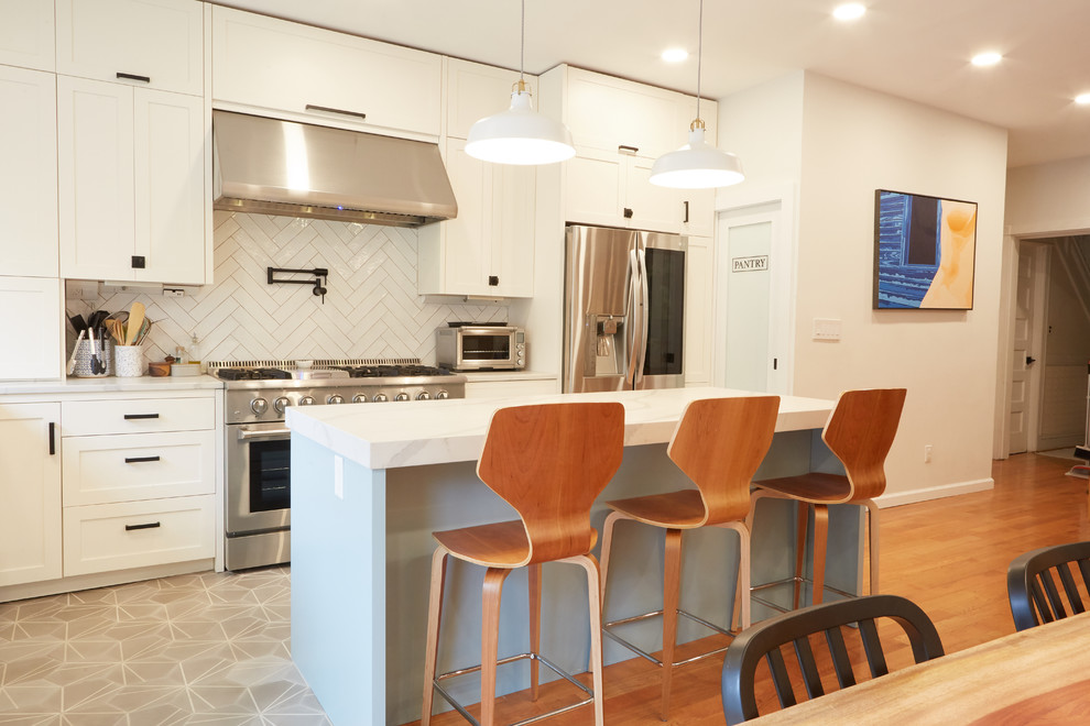 Mid-sized transitional u-shaped eat-in kitchen in New York with a farmhouse sink, recessed-panel cabinets, white cabinets, quartzite benchtops, white splashback, ceramic splashback, stainless steel appliances, medium hardwood floors, with island, multi-coloured floor and white benchtop.