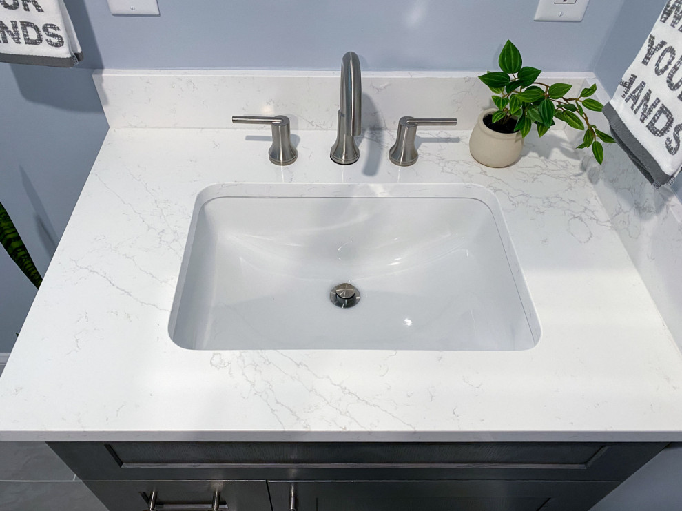 Inspiration for a transitional white tile and ceramic tile porcelain tile, gray floor and single-sink corner shower remodel in Boston with shaker cabinets, gray cabinets, a one-piece toilet, gray walls, an undermount sink, quartz countertops, a hinged shower door, white countertops and a built-in vanity