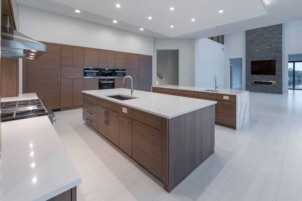 Design ideas for an expansive contemporary kitchen in Orlando with an integrated sink, flat-panel cabinets, light wood cabinets, quartzite benchtops, grey splashback, stone slab splashback, black appliances, porcelain floors, multiple islands, grey floor and grey benchtop.