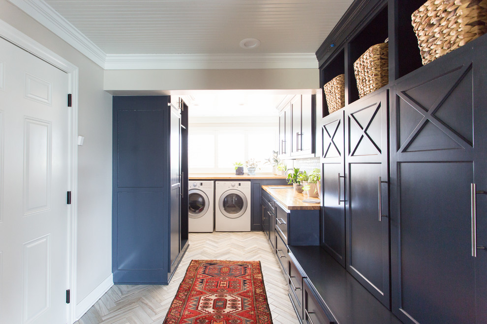 Mid-sized beach style utility room in Kansas City with blue cabinets, wood benchtops, grey walls, a side-by-side washer and dryer and grey floor.
