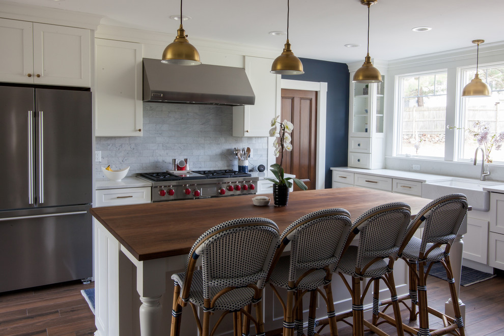 Inspiration for a large transitional dark wood floor kitchen remodel in Boston with a farmhouse sink, shaker cabinets, white cabinets, quartz countertops, stainless steel appliances, an island, white countertops and gray backsplash
