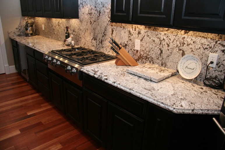 Example of a mid-sized transitional dark wood floor and brown floor kitchen design in Miami with raised-panel cabinets, black cabinets, granite countertops, gray backsplash, stone slab backsplash and stainless steel appliances