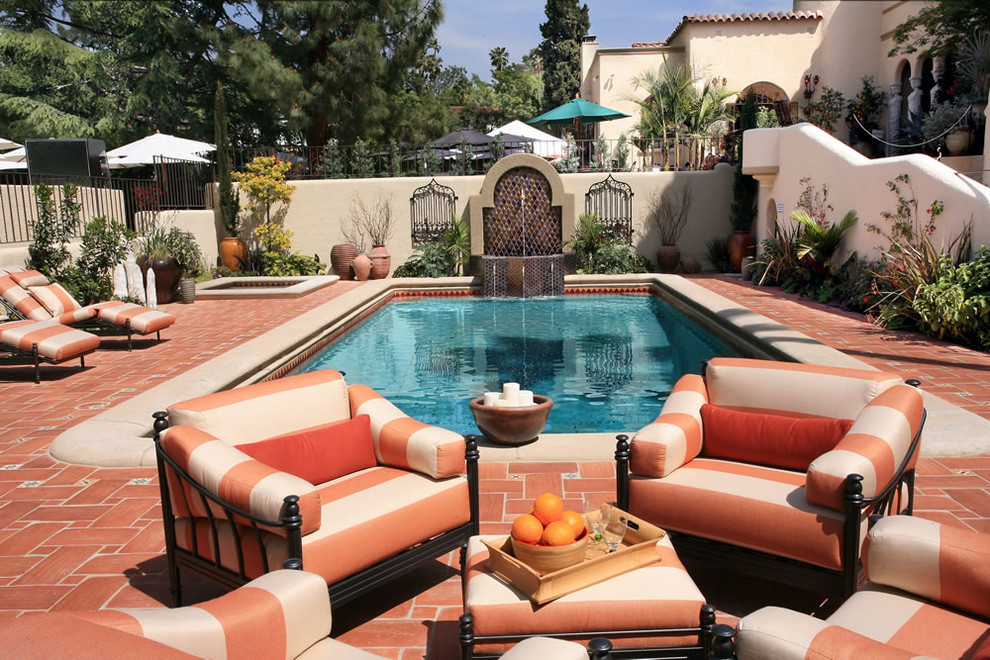 This is an example of a mid-sized mediterranean backyard rectangular lap pool in Orange County with a hot tub and brick pavers.