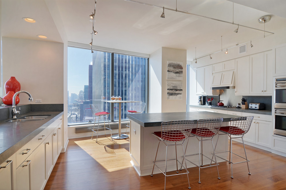 This is an example of a contemporary eat-in kitchen in Chicago with a double-bowl sink, shaker cabinets, white cabinets, grey splashback, stainless steel appliances, medium hardwood floors and with island.