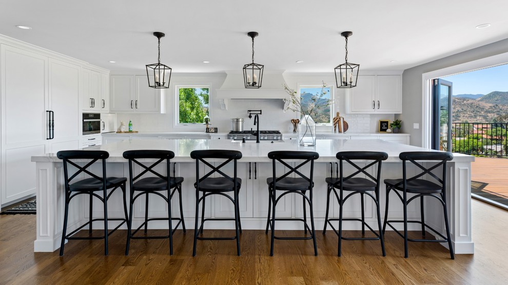 Inspiration for a large transitional single-wall medium tone wood floor and brown floor eat-in kitchen remodel with a single-bowl sink, raised-panel cabinets, white cabinets, quartzite countertops, white backsplash, ceramic backsplash, stainless steel appliances, an island and white countertops