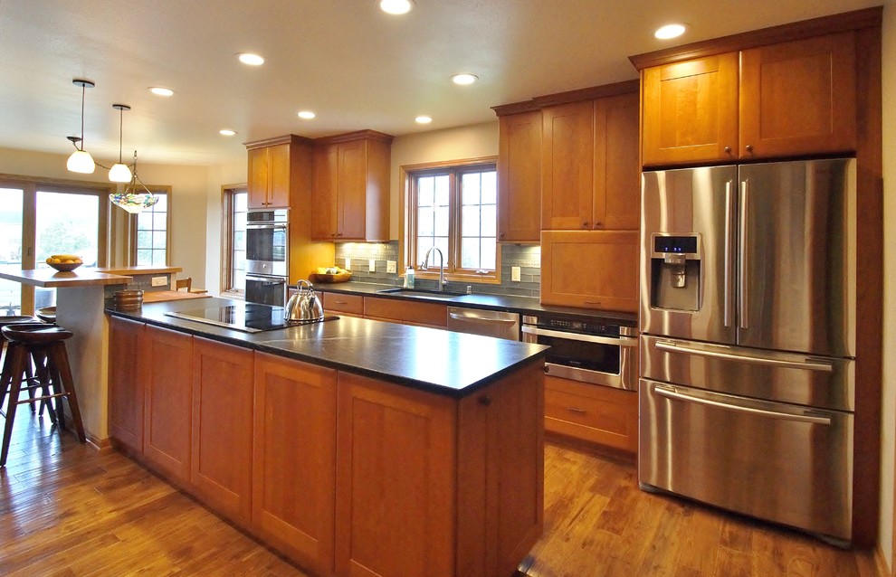 Inspiration for a transitional galley medium tone wood floor eat-in kitchen remodel with a double-bowl sink, recessed-panel cabinets, medium tone wood cabinets, soapstone countertops, stainless steel appliances and an island