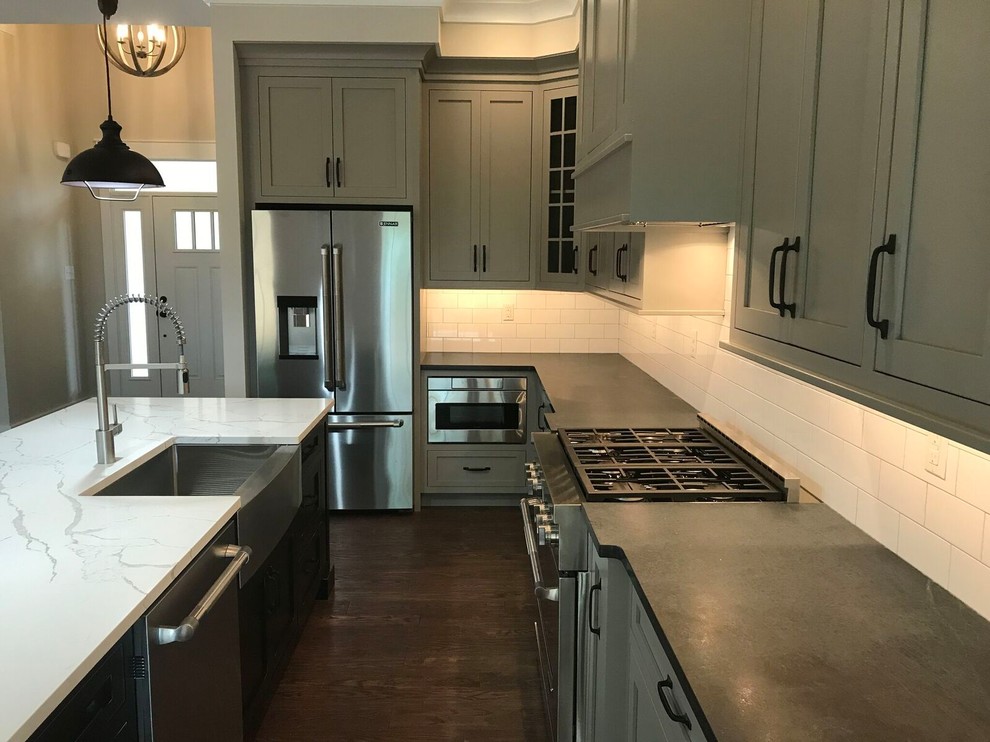 Photo of a mid-sized contemporary l-shaped open plan kitchen in Philadelphia with a farmhouse sink, shaker cabinets, grey cabinets, marble benchtops, white splashback, subway tile splashback, stainless steel appliances, dark hardwood floors, with island and brown floor.