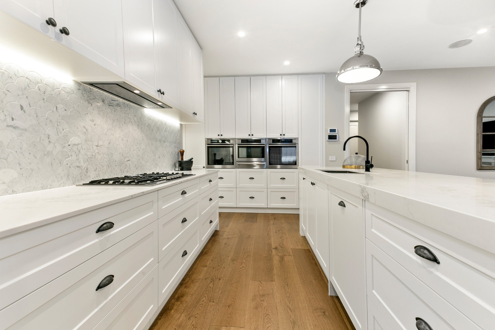 Design ideas for a large transitional galley open plan kitchen in Melbourne with an undermount sink, shaker cabinets, white cabinets, quartz benchtops, grey splashback, marble splashback, white appliances, linoleum floors, with island and brown floor.