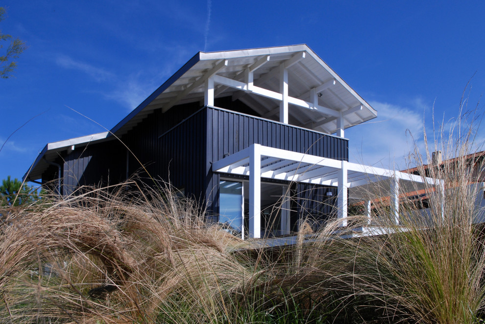 Inspiration for a mid-sized beach style two-storey black exterior in Montpellier with wood siding and a gable roof.