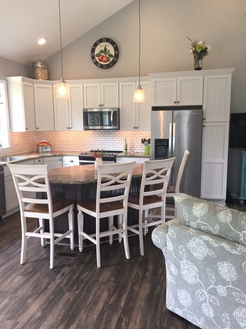 This is an example of a mid-sized beach style l-shaped eat-in kitchen in Baltimore with an undermount sink, flat-panel cabinets, white cabinets, laminate benchtops, white splashback, subway tile splashback, stainless steel appliances, dark hardwood floors, with island and brown floor.