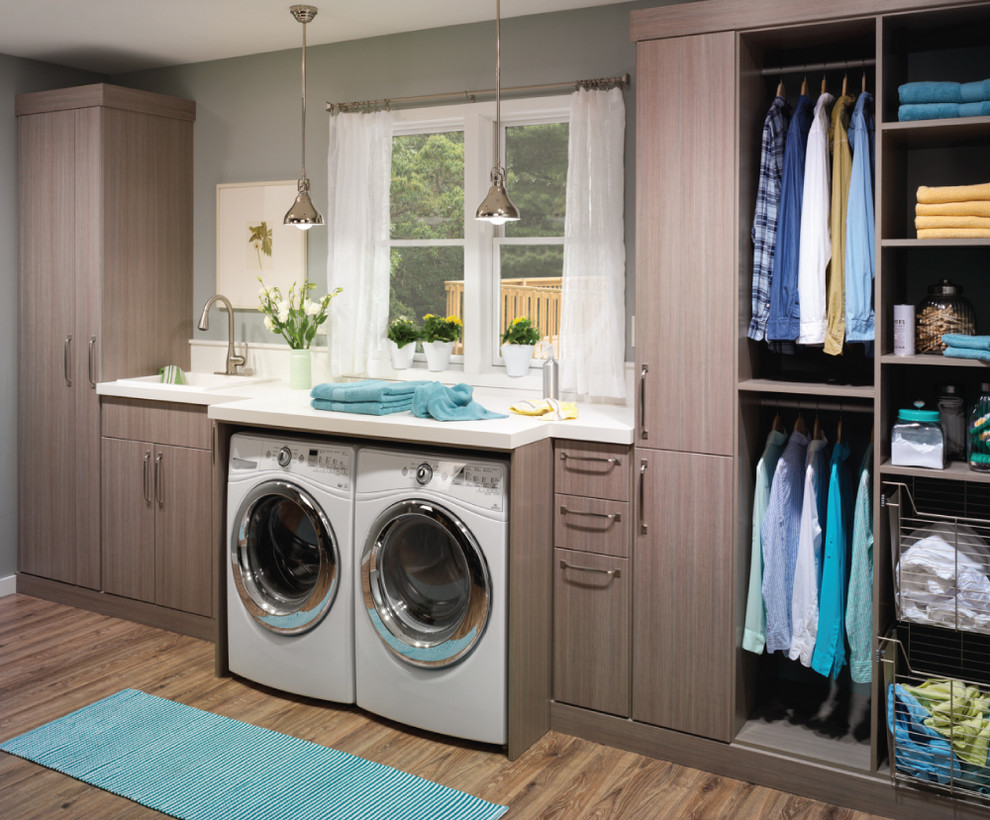 This is an example of a mid-sized industrial single-wall dedicated laundry room in New York with a drop-in sink, flat-panel cabinets, limestone benchtops, a side-by-side washer and dryer, grey walls, light hardwood floors and grey cabinets.