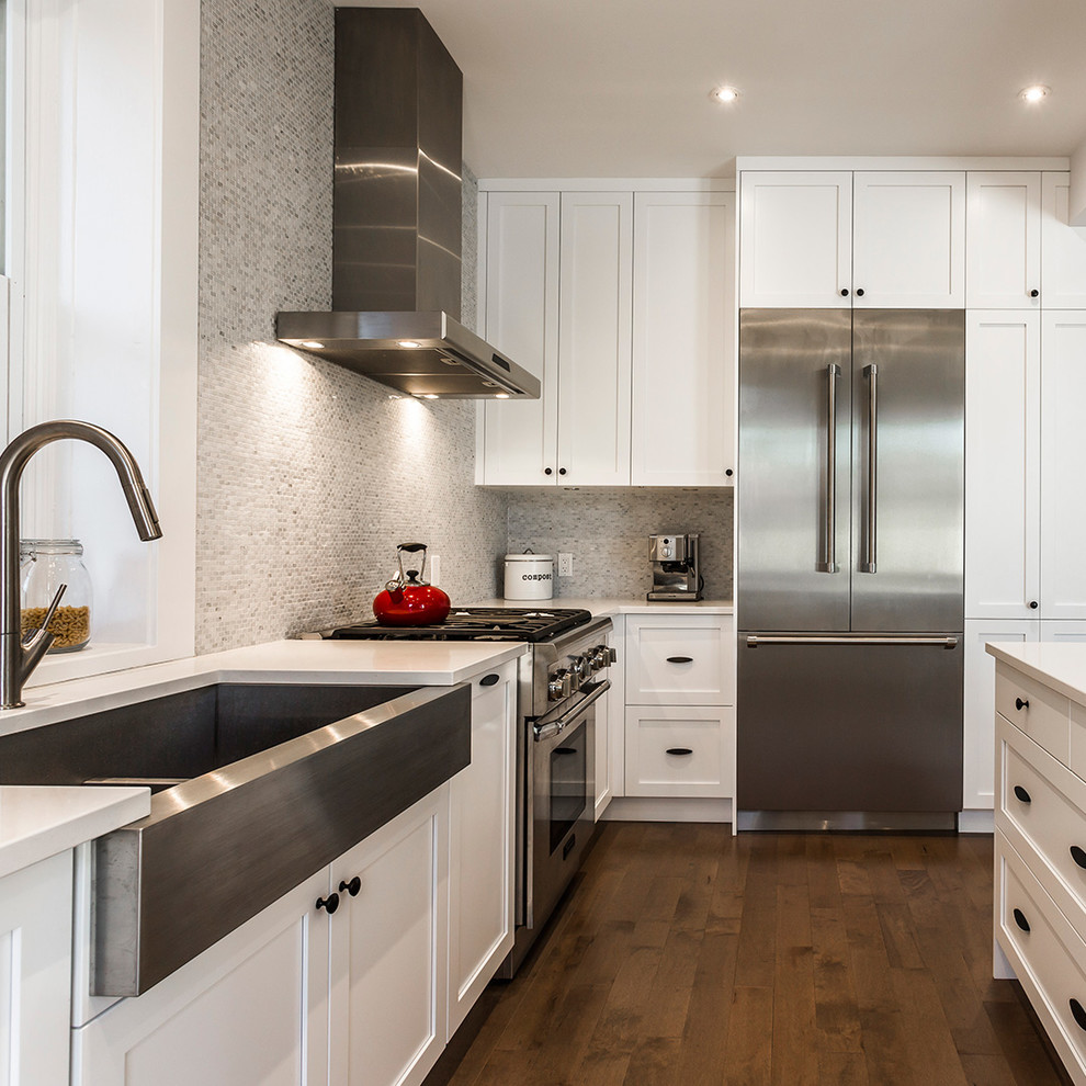 Example of a large transitional l-shaped light wood floor and brown floor open concept kitchen design with a farmhouse sink, shaker cabinets, white cabinets, gray backsplash, stainless steel appliances and an island