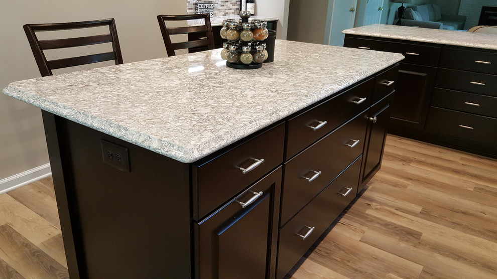 Mid-sized transitional l-shaped light wood floor and brown floor eat-in kitchen photo with an undermount sink, raised-panel cabinets, dark wood cabinets, quartz countertops, multicolored backsplash, cement tile backsplash, stainless steel appliances and an island