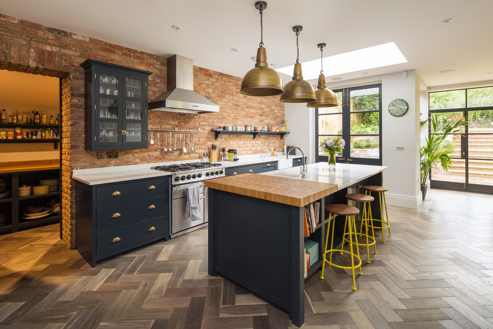 Inspiration for a country galley open plan kitchen in London with a farmhouse sink, glass-front cabinets, blue cabinets, brick splashback, stainless steel appliances, medium hardwood floors and with island.