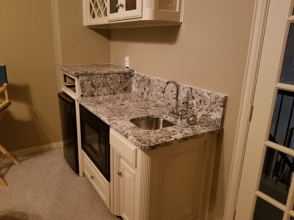 This is an example of a small traditional single-wall wet bar in Dallas with an undermount sink, glass-front cabinets, beige cabinets, granite benchtops, carpet, brown floor and grey benchtop.