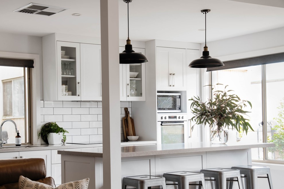 Design ideas for a country open plan kitchen with an undermount sink, shaker cabinets, white cabinets, quartz benchtops, white splashback, subway tile splashback, stainless steel appliances, laminate floors, with island, brown floor and grey benchtop.